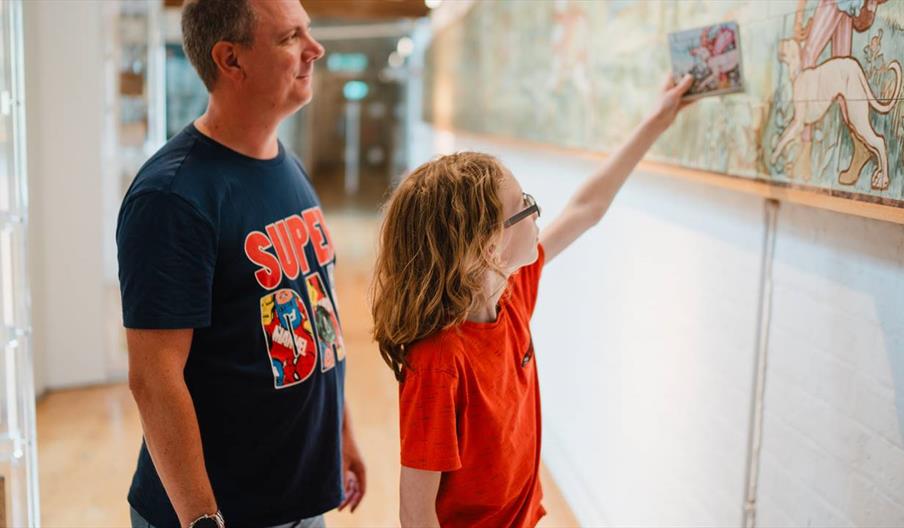 Father and son. The son is holding up a photo of a tile next to a decorative tile panel.