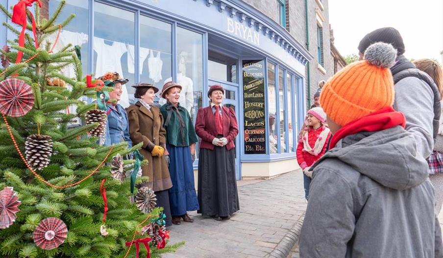 Victorian carollers signing beside a Christmas tree