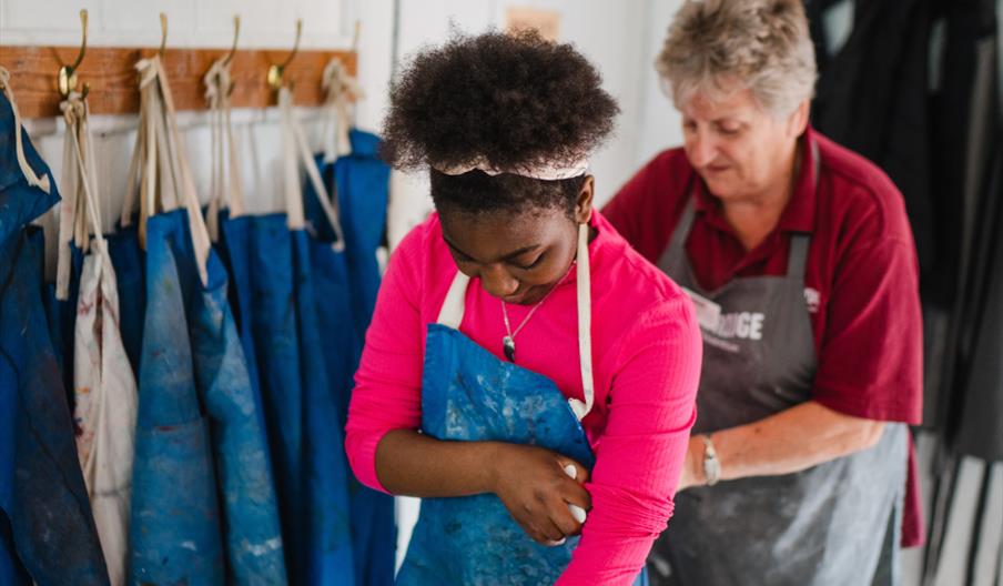 Young girl putting on a blue apron at Coalport China Museum