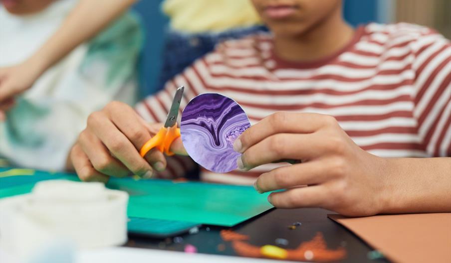 A boy cutting out a planet shape which he has decorated using marbling inks.