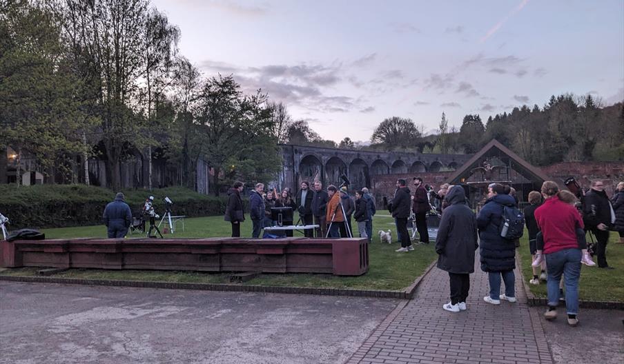 A photo of everyone gathering up to see the stars through a telescope.