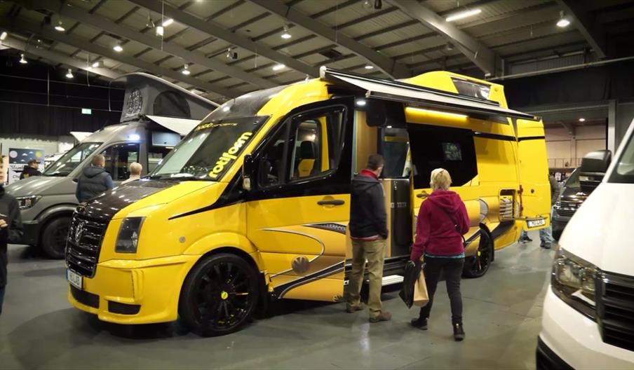 A yellow and black VW camper shown at a previous show