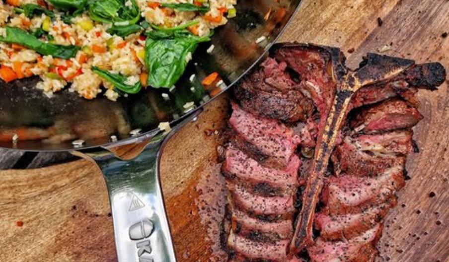 Beef on a wooden chopping block with a pan of side