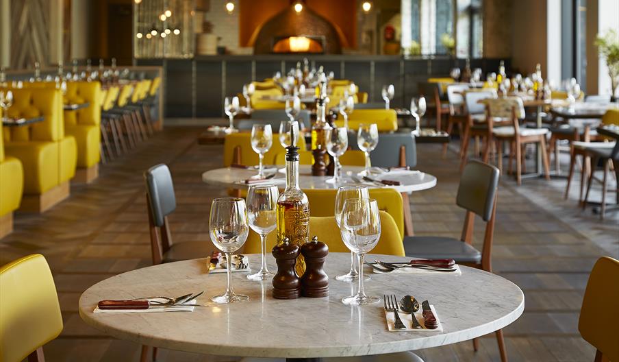 At Wildwood Telford, a modern restaurant with neatly arranged tables set with wine glasses, cutlery, and condiments, yellow chairs add to the cozy atm