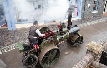 Man on a steam roller driving through Victorian streets.