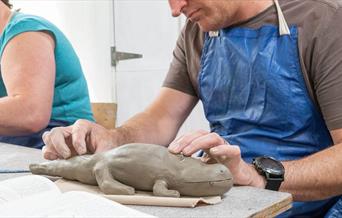 A man in a blue apron building with clay