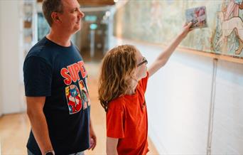 Father and son. The son is holding up a photo of a tile next to a decorative tile panel.