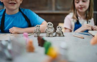 Three small clay figures of people with a boy and girl in the background.
