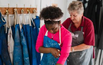 Young girl putting on a blue apron at Coalport China Museum