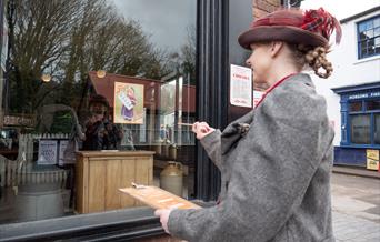 A Victorian woman pointing at a window as she follows a chocolate trail.