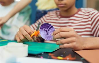 A boy cutting out a planet shape which he has decorated using marbling inks.