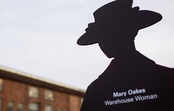 A black cut out of a woman in a hat, white text on it reads Mary Oakes Warehouse woman.