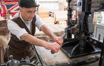 A man dressed in Victorian clothing is using a manual printing press