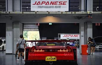 A photo from the inside of a previous show showing visitors and a red performance Honda on display