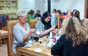 a group taking part in late night pottery painting, the social craft.