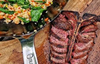 Beef on a wooden chopping block with a pan of side