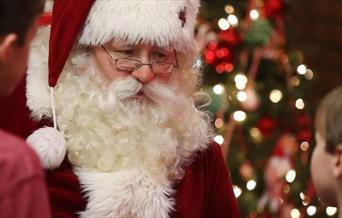 Santa in his red suit, glasses and beard meeting children
