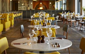 At Wildwood Telford, a modern restaurant with neatly arranged tables set with wine glasses, cutlery, and condiments, yellow chairs add to the cozy atm