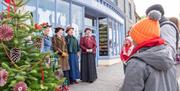 Victorian carollers signing beside a Christmas tree