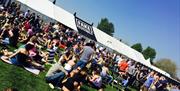 Festival goers sat on grass outside music tent on a sunny day