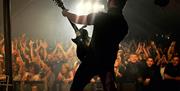 Artist on stage playing guitar, performing to festival crowd