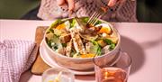 A woman at Wildwood Restaurants delicately eats a chicken caesar salad using a fork.