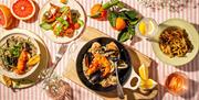 A summer table set with various dishes, including seafood risotto, a salad, grilled vegetables, a side dish of zucchini fries, and a grapefruit half f