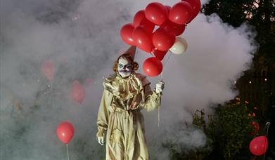 Clown holding balloons, surrounded by fog.