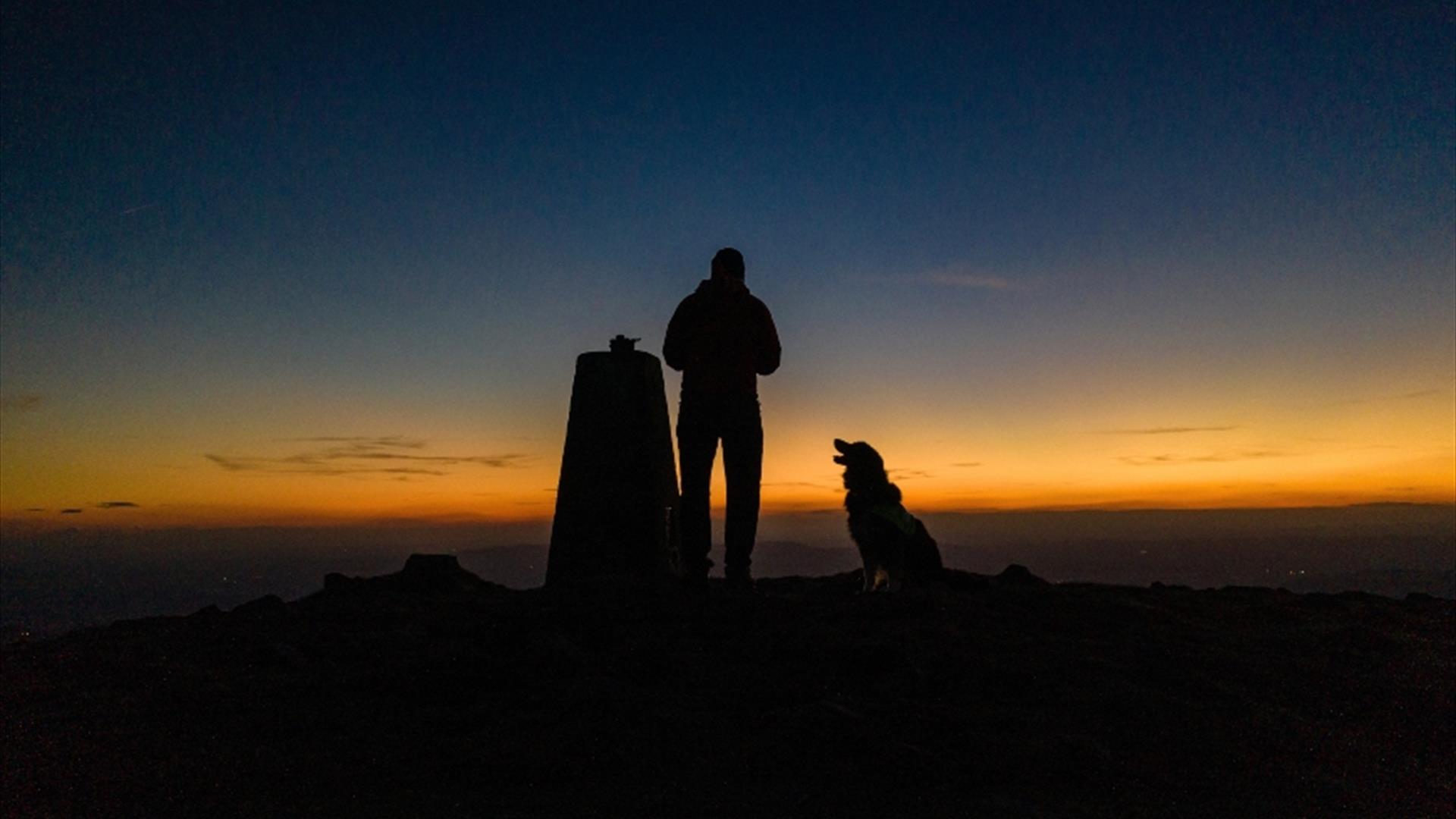 Man and his dog watching the sunrise in The Wrekin