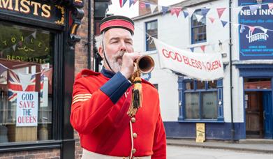A Victorian soldier in ceremonial uniform playing a trumpet in the streets of a historic town
