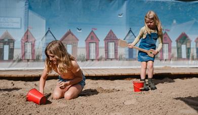 Two girls are playing in the sand with buckets and spades