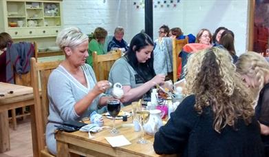 a group taking part in late night pottery painting, the social craft.