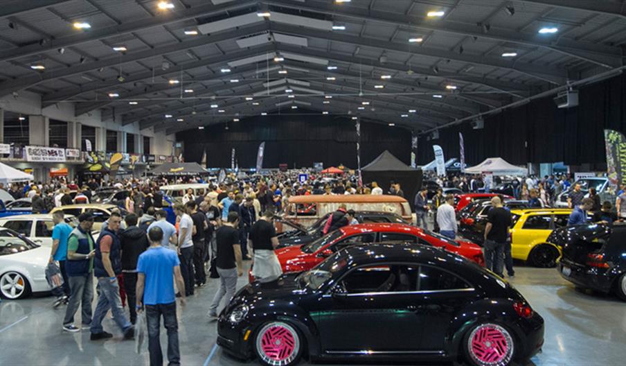 A packed exhibition hall from a previous show, with display cars and visitors