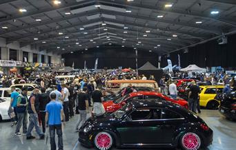 A packed exhibition hall from a previous show, with display cars and visitors