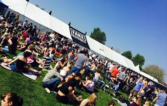 Festival goers sat on grass outside music tent on a sunny day
