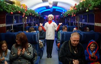 Female Chef in Train Carriage surrounded by customers sat down