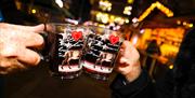Two people saying cheers with glass mugs full of gluhwein
