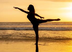 Silhouette of a lady doing yoga on a beach at sunset