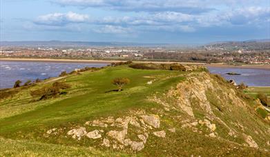 View over the top of a grass-topped rocky cliff with sea on either side and a shoreline in the background