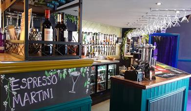 An empty bar with wine glasses hanging from the ceiling and wine bottles in the foreground