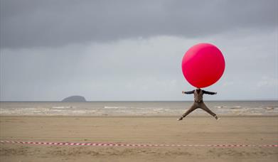A man on the beach with a giant balloon over his head.