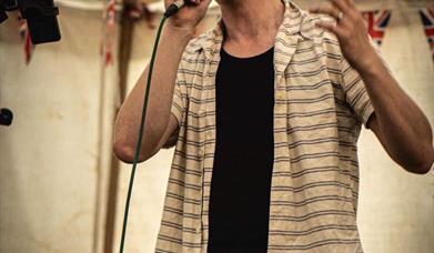 Photograph of James Anthony singing into a microphone on stage with event information.