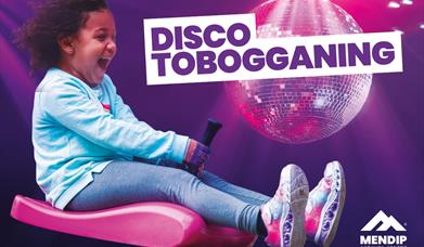 Little girl looking happy and excited riding a zibob toboggan. Background display a disco ball on a purple background, with light glowing down onto th