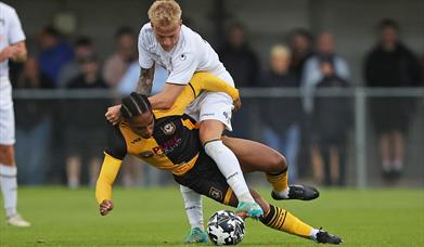 A Newport County footballer about to fall to the ground as he's tackled by a Weston-super-Mare footballer