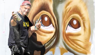A street artist with spray can working on a giant mural of a monkey