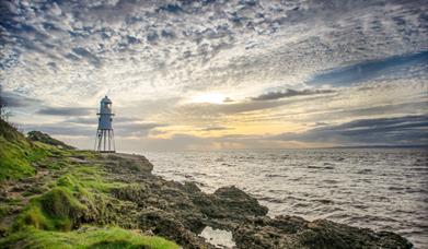 A distinctive lighthouse sitting on rocks beneath a sunset