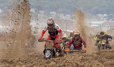Sand flies up as three motorbike riders struggle through sand in a beach race