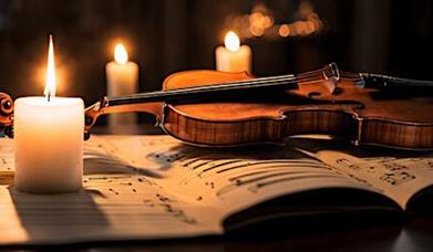 A burning candle on top of some sheet music with a violin