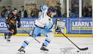 A Bristol Pitbulls ice hockey player in their light blue and white kit comes away with the puck