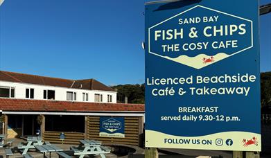 Close up image of the Sand Bay Fish & Chip shop sign against a blue sky with the premises in the background